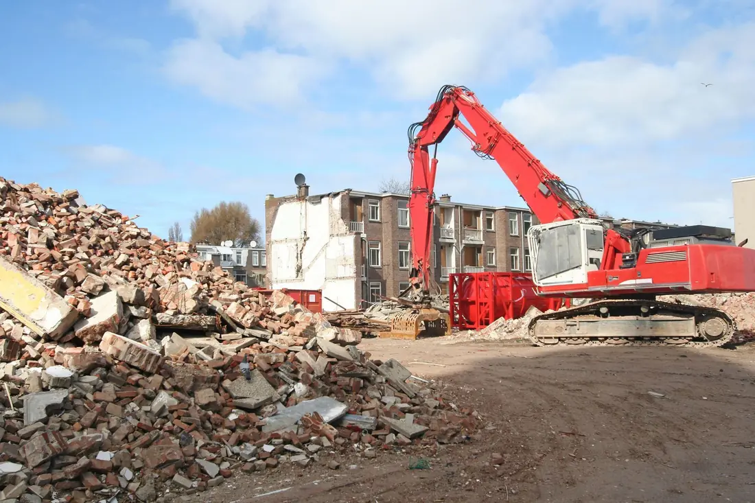 Red excavator demolishing a building beside a rubble pile