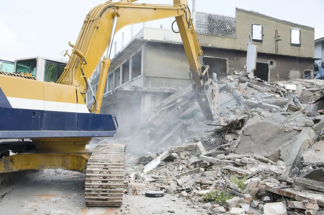 Yellow excavator demolishing a collapsed building