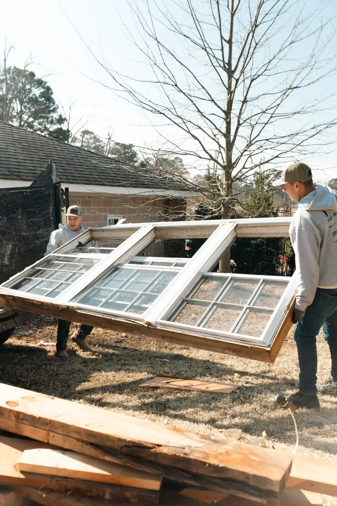 Two workers carrying a large white-framed window out of a home