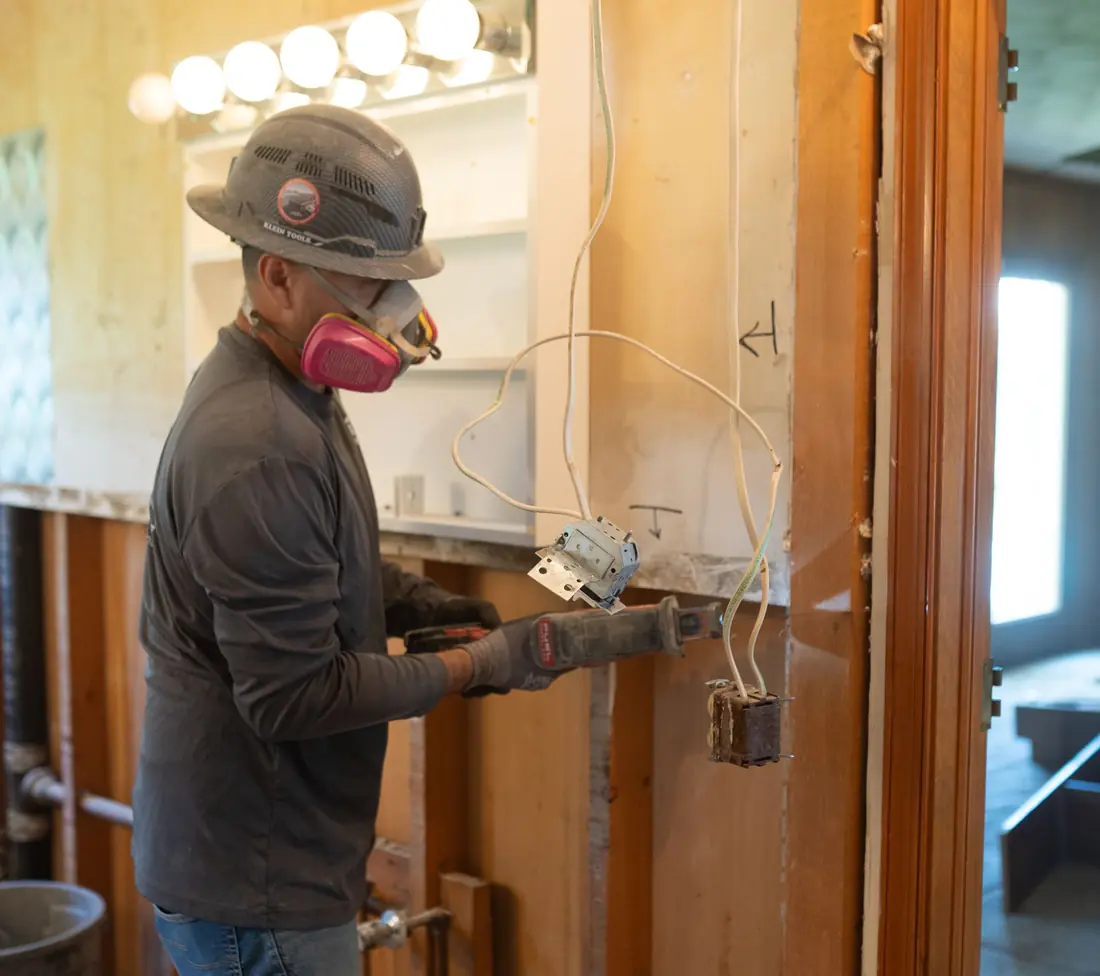 Worker gutting interior walls and wiring during a demolition job